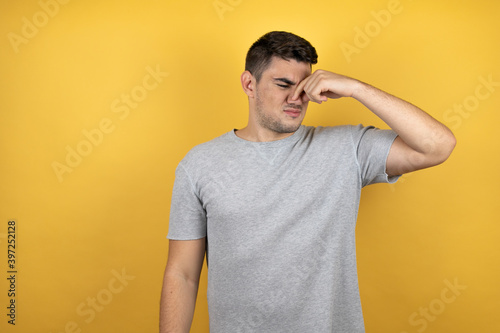 Young handsome man wearing a casual t-shirt over isolated yellow background thinking looking tired and bored with hands on head