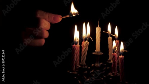 A person lights candles on the Jewish holiday of Hanukkah. On a black isolated background close up in 4K without a face. photo