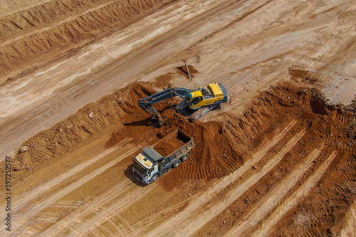 quarry development for clay extraction. overburden works. excavator breaks up the topsoil to extract clay and loads into grey truck. drone photo. aerial view