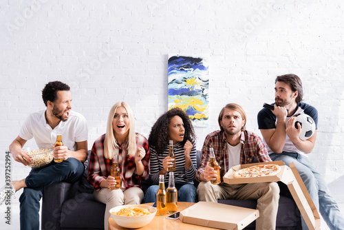 worried and excited football fans watching championship with beer  pizza and chips at home