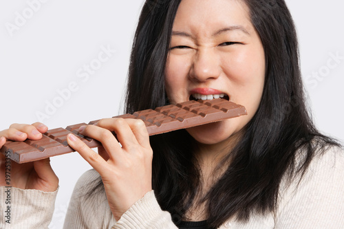 Portrait of a young woman eating a large chocolate bar over light gray background