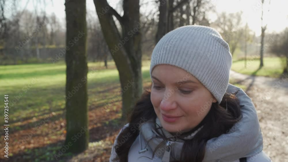 Beautiful woman in warm coat walking in autumn park, brunette lady strolling on a cold sunny day.
