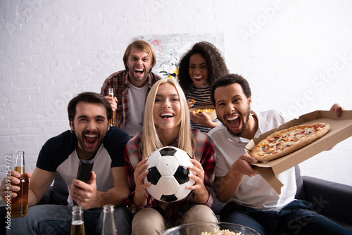 excited multiethnic friends watching football championship with beer and pizza  blurred foreground