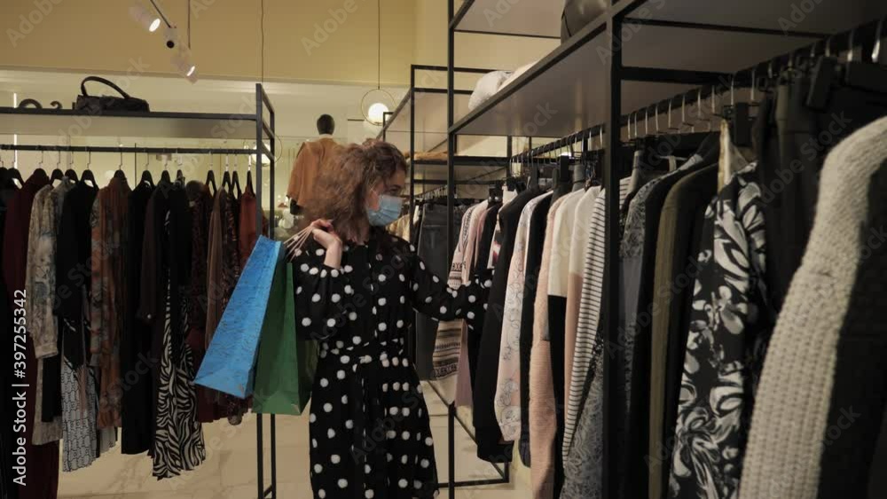 Beautiful girl in a medical mask is shopping in a stylish boutique during the covid pandemic coronavirus. Beautiful girl in a medical mask is shopping in a stylish boutique during the covid pandemic coronavirus.