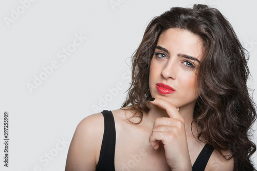 Portrait of a thoughtful young woman with hand on chin over gray background