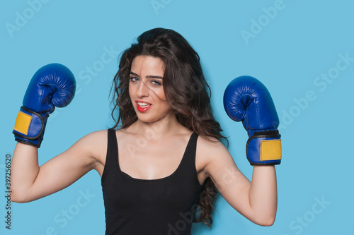 Portrait of a beautiful young female boxer raising arms in victory against blue background