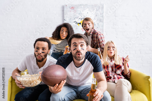 Canvas Print shocked multicultural friends with painted faces watching rugby championship at