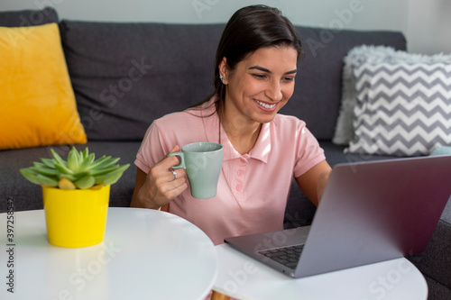 A young woman is drinking coffee and working from home on a laptop. 