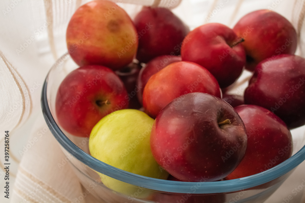 Lots of ripe apples in a transparent cup against the background of beige fabric