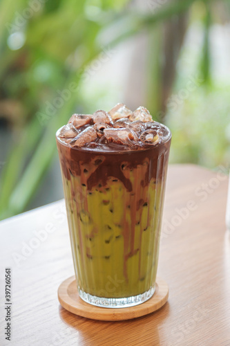 A glass of iced latte fusion two layers matcha and chocolate on wooden table,  homemade latte refreshment in cafe background.