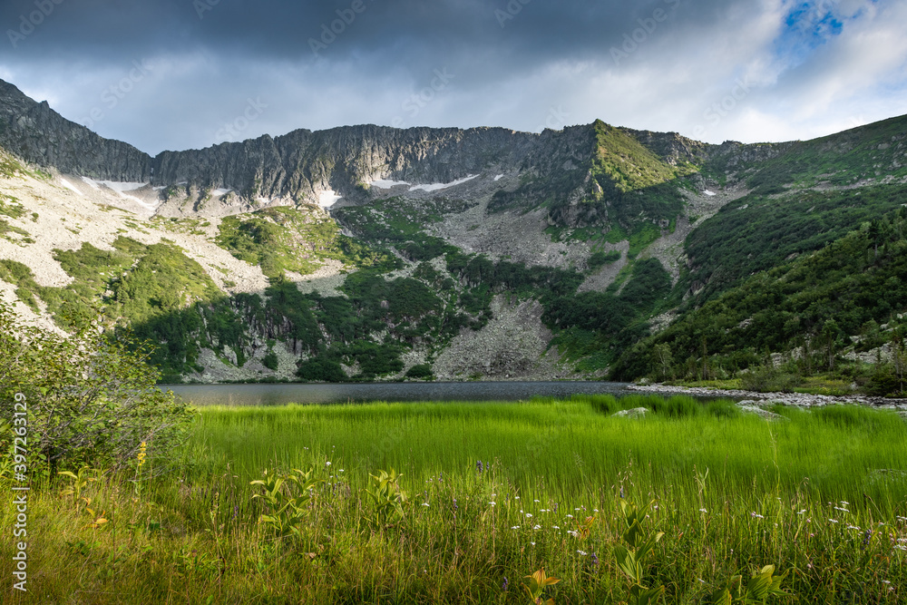 Lake at foot of mountain range. River in mountain valley along rocks. Summer morning in mountains of Siberia Lake at foot of mountain range. River in mountain valley along rocks. Summer morning in mountains of Siberia