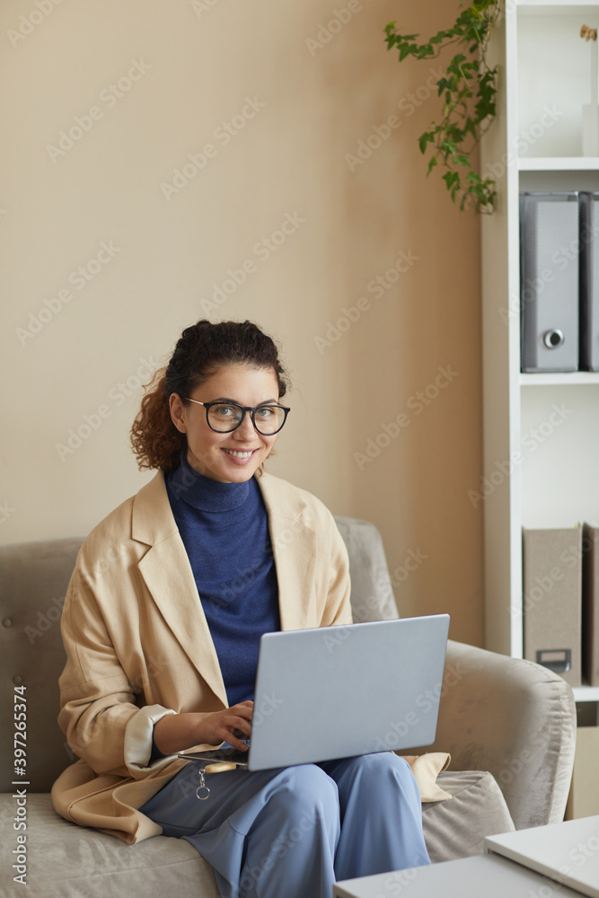Portrait of young businesswoman in eyeglasses sitting on sofa and working online on laptop computer Portrait of young businesswoman in eyeglasses sitting on sofa and working online on laptop computer