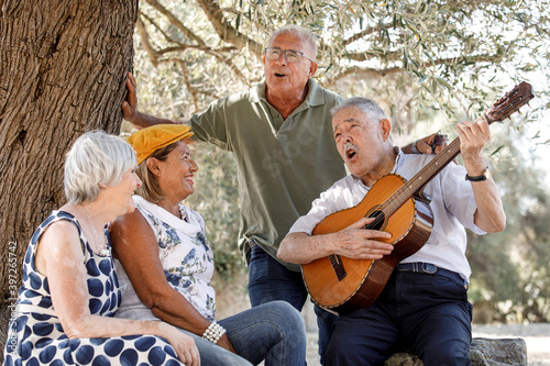 Anziano Ottantenne insieme a un suo amico  suona una serenata a due anziane signore tutti seduti  sotto un albero di ulivo in campagna photo