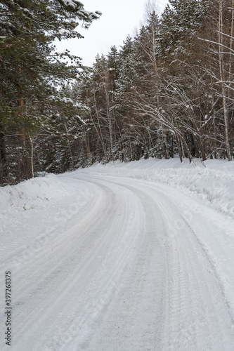 Snow road in winter pine forest. Ice and snowstorm on a country road. Clearing the road from snowdrifts.