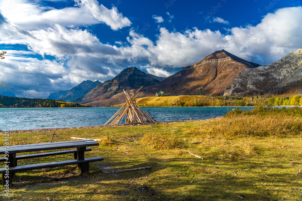 Driftwood Beach, Middle Waterton Lake lakeshore in autumn foliage season morning. Blue sky, white clouds over mountains in the background. Landmarks in Waterton Lakes National Park, Alberta, Canada.