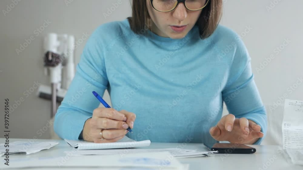 Young woman sits at the table, studies utility bills and sums up costs, money manages finances, family budget