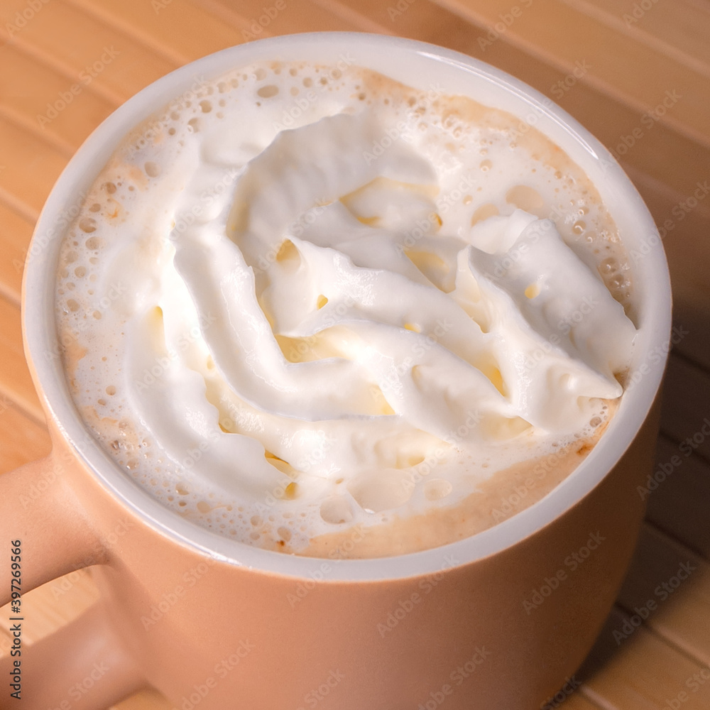 Beige Cup of aromatic coffee with cream on a wooden napkin. Winter holiday at home or in a cozy cafe. Close-up photo. Beige Cup of aromatic coffee with cream on a wooden napkin. Winter holiday at home or in a cozy cafe. Close-up photo.