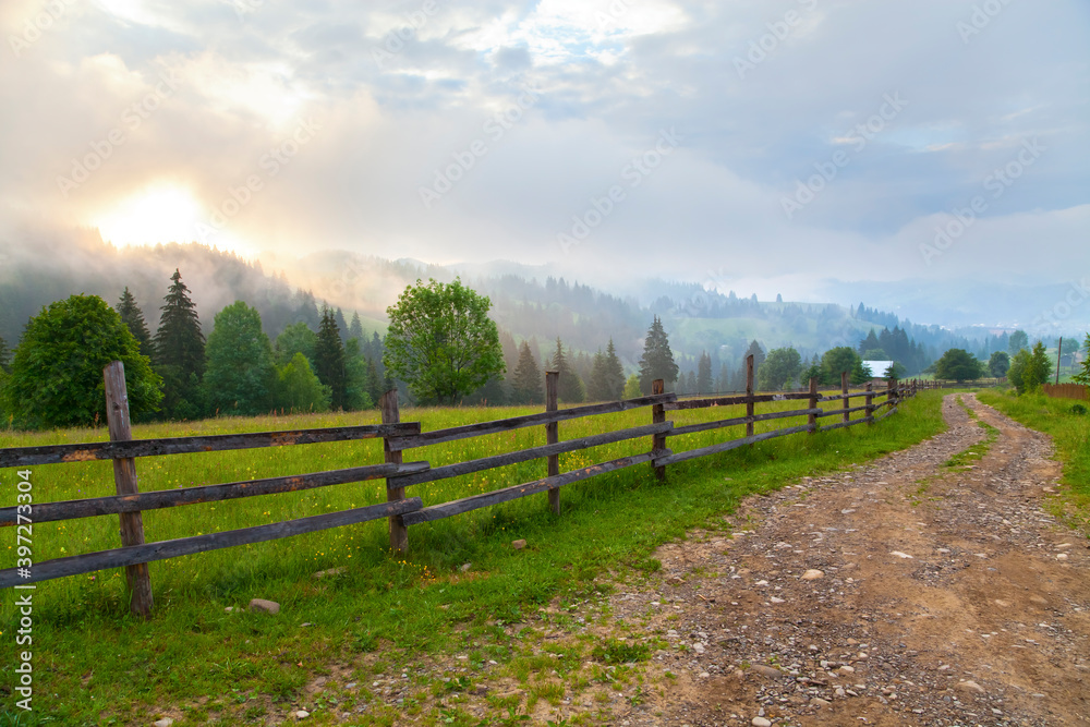 Mountain meadow with wooden fence along a road. view of the village and mountains in deep fog. Ukraine, Verkhovyna.