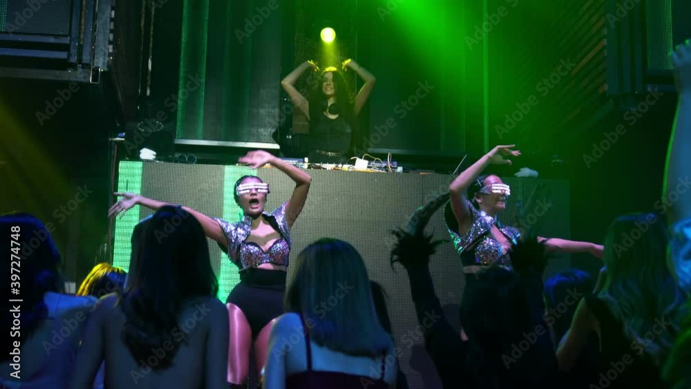Group of people dance in disco night club to the beat of music from DJ on stage . New year night party and nightlife concept .
