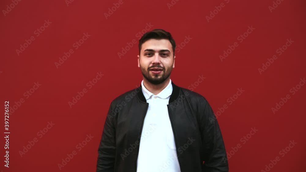 Happy bearded man stands on a red background and shows his finger to the camera with a smile on his face. Happy bearded man stands on a red background and shows his finger to the camera with a smile on his face.