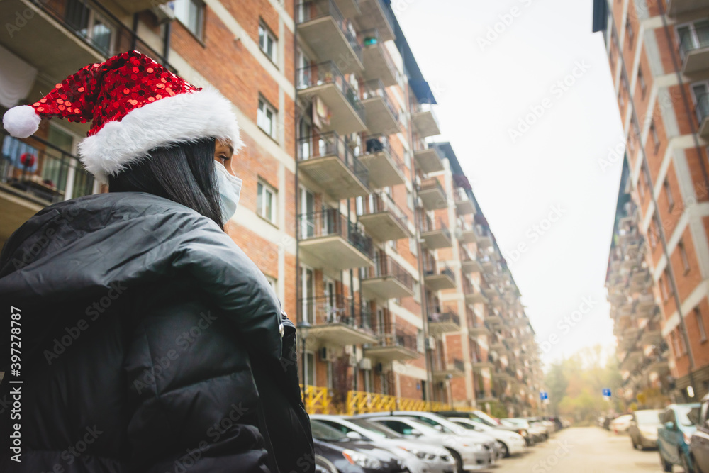 Obraz premium Female person in holiday season looks to the right with street view and houses in the background. Xmas at home on quarantine and curfew on Christmas.