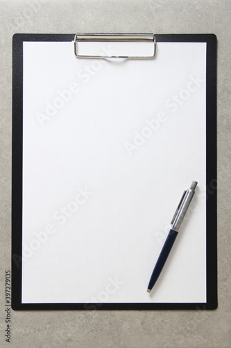 Template of white paper with a ballpoint pen on light grey concrete background in a black tablet with a clip. Concept of new idea, business plan and strategy, with empty space for text