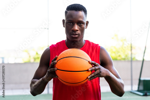 Determined male basketball player standing with ball on playground in summer and looking at camera photo