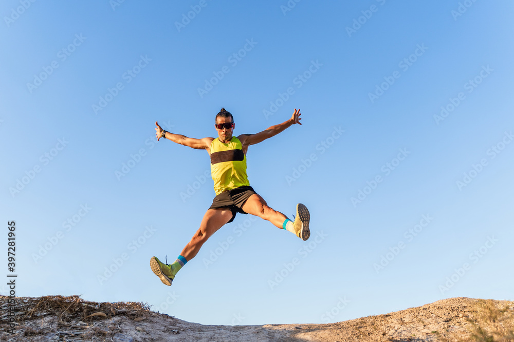 From below full body of energetic athletic male in sportswear and sunglasses jumping high with outstretched arms against cloudless blue sky From below full body of energetic athletic male in sportswear and sunglasses jumping high with outstretched arms against cloudless blue sky