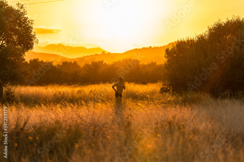 Side view of unrecognizable sportsman with naked torso running along dry meadow in countryside during cardio training at sundown in summer