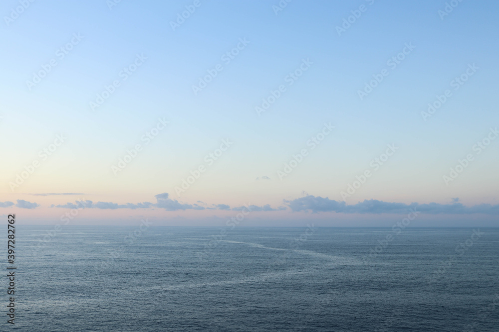 Fototapeta premium Calm sea with sunset sky and sun through the clouds over