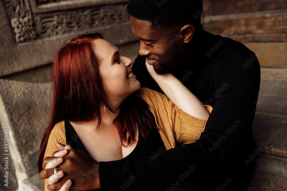 Adorable couple cuddling near the house, walking at the city, charming African American husband gently hug beautiful wife, overjoyed woman smiling, tender moments concept Adorable couple cuddling near the house, walking at the city, charming African American husband gently hug beautiful wife, overjoyed woman smiling, tender moments concept