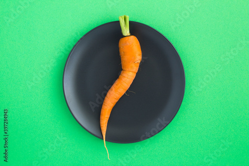 Curved carrot in the black plate in the center of the green background