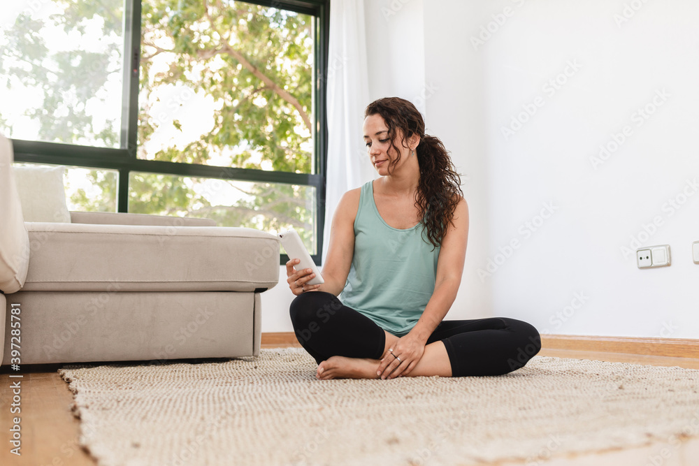 Calm female in domestic outfit sitting with crossed legs on floor and messaging on social media via mobile phone at weekend Calm female in domestic outfit sitting with crossed legs on floor and messaging on social media via mobile phone at weekend