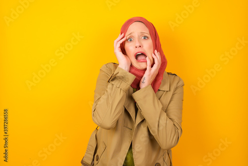 Photography Young gloomy Young caucasian Muslim woman wearing hijab standing against yellow wall, hiding face with hands pouting and crying, standing upset and depressed complaining about job problem
