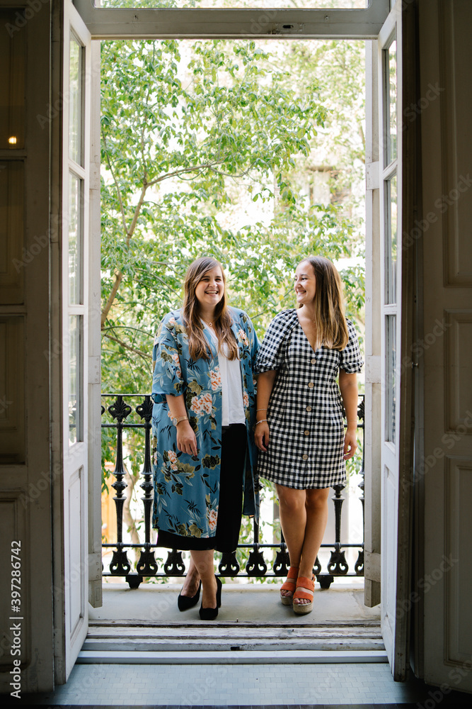 Cheerful female friends in stylish outfit standing on balcony together and enjoying weekend Cheerful female friends in stylish outfit standing on balcony together and enjoying weekend