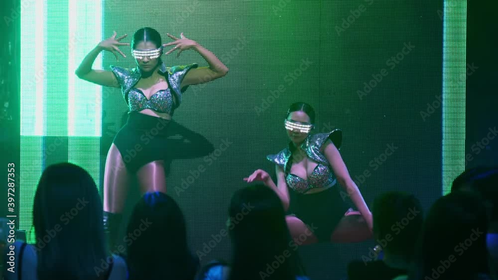 Group of people dance in disco night club to the beat of music from DJ on stage . New year night party and nightlife concept .
