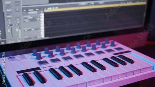 Male hands recording music, playing electronic keyboard, midi keys on the table with neon lights. Closeup of male hands composing music in night, music sequencer and midi controller