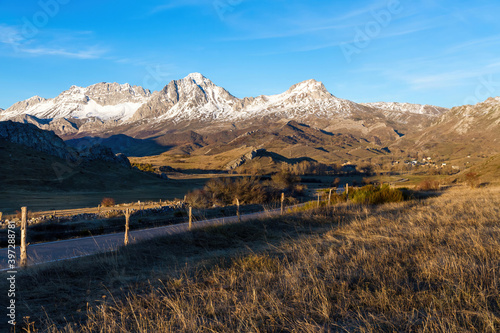 Vista de paisaje invernal con carretera de acceso a un valle rodeado de altas montañas, picos nevados y pueblo
