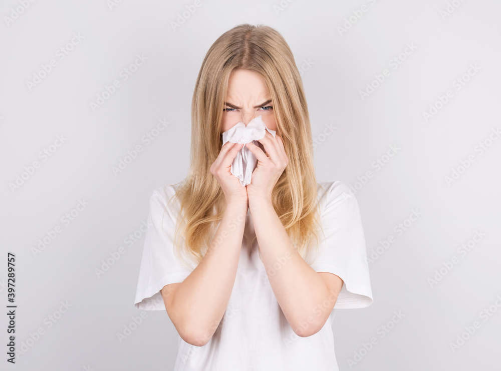 Studio portrait of cute unhealthy caucasian woman with paper napkin sneezing due to allergy, flu or cold Studio portrait of cute unhealthy caucasian woman with paper napkin sneezing due to allergy, flu or cold