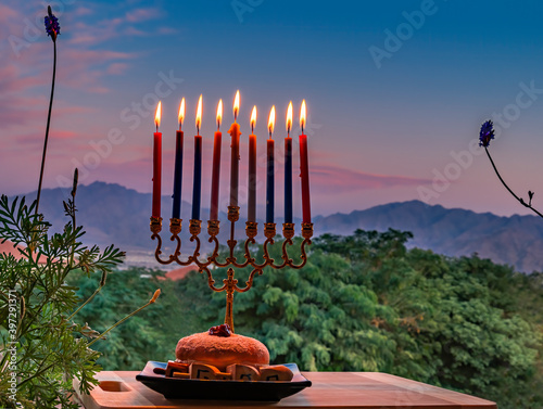 Burning candles, menorah and sweet donates on plate with wooden dreidels for ...