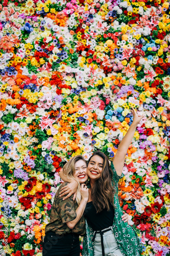 Cheerful female friends embracing while standing against colorful flowers