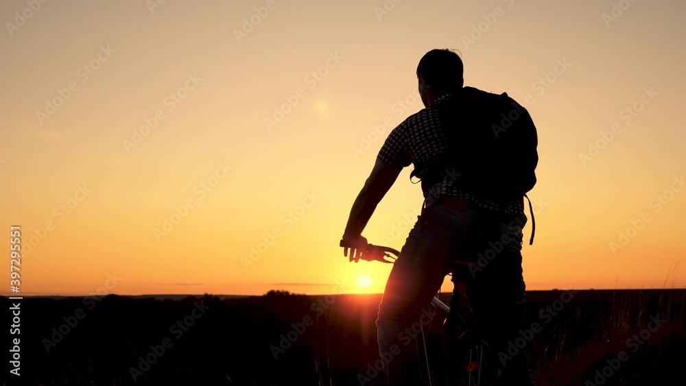 Tourist a healthy young man rides a Bicycle to edge of hill, enjoying nature and sun. A free traveler travels with bicycle at sunset. concept of adventure and travel. lonely cyclist resting in park.