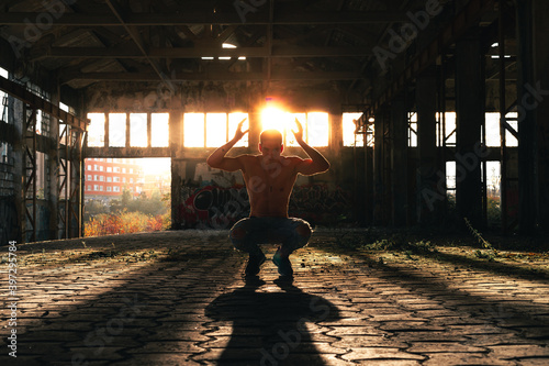 Fitness man posing in a ruined industry pavillion with the sunlight at the back.