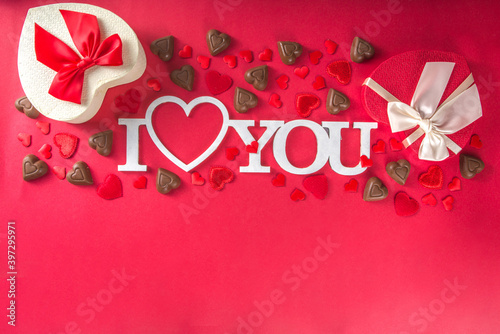 Red hearts, gift with ribbon and chocolates hearts flat lay, Valentine day and love background. Valentine's hearts ornament on red backdrop, with word leter i love you above