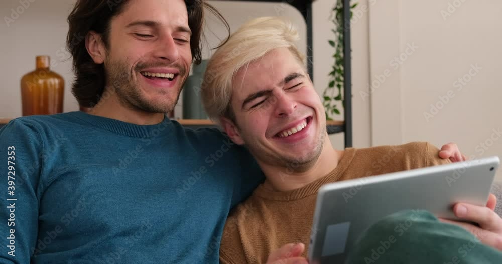 Gay couple having fun using digital tablet sitting on sofa at home