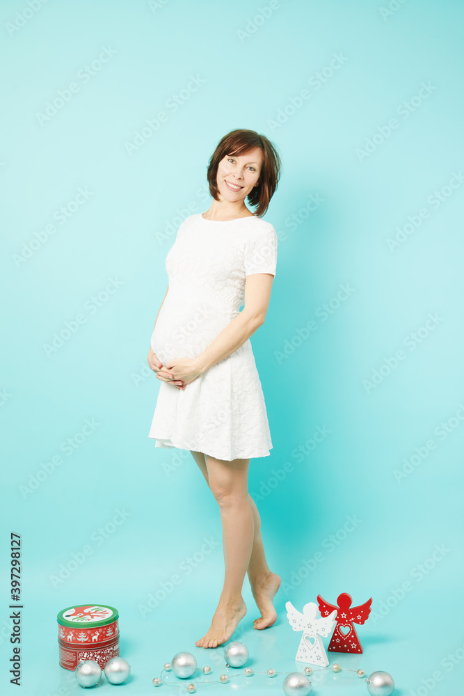 Beautiful caucasian pregnant woman with Christmas toys and ornaments isolated on blue background. Beautiful caucasian pregnant woman with Christmas toys and ornaments isolated on blue background.