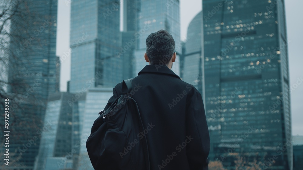 Rear view of a young unrecognizable businessman walking slowly and looking at skyscrapers in a summer evening. Moscow city background. 