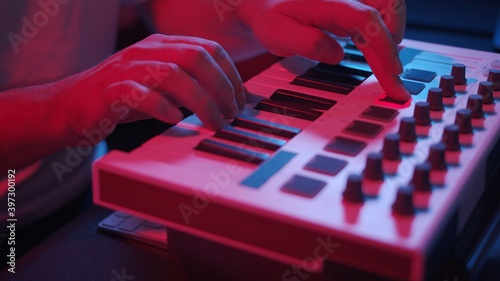 Male hands recording music, playing electronic keyboard, midi keys on the table with neon lights. Closeup of male hands composing music in night using midi controller
