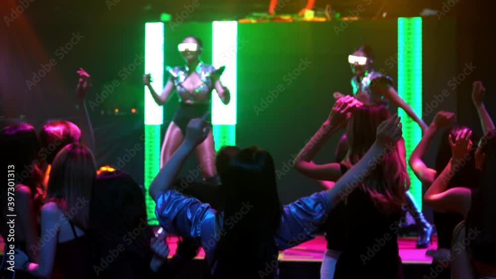 Group of people dance in disco night club to the beat of music from DJ on stage . New year night party and nightlife concept .
