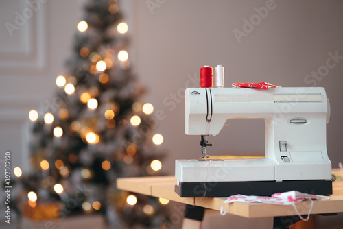 A commercial shot of a sewing machine with two red and white threads on the top and a Christmas tree on the background